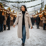 Woman in a long coat walking through a snowy outdoor market with lights and people in the background.