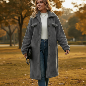 Woman wearing a long gray coat in an outdoor setting with trees and grass.