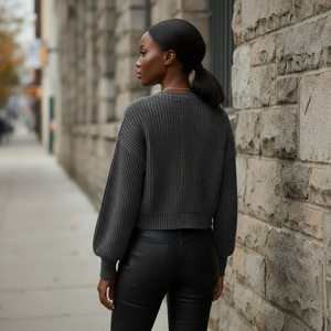 Woman in a dark gray sweater and black pants standing against a stone wall.