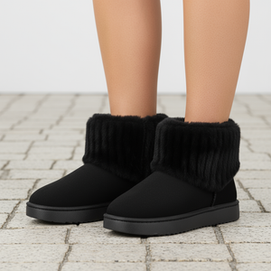 Black slip-on boots with fuzzy texture worn by a person on a stone pavement.