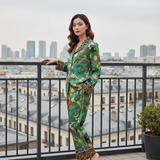 Woman in a green patterned outfit standing on a balcony with cityscape in the background