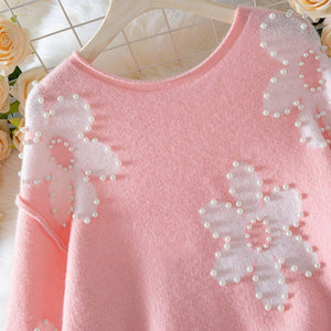 Pink sweater with floral embellishments on a hanger against a floral background