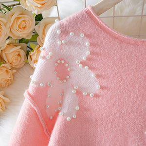 Pink sweater with a white bow and pearl details against a floral background