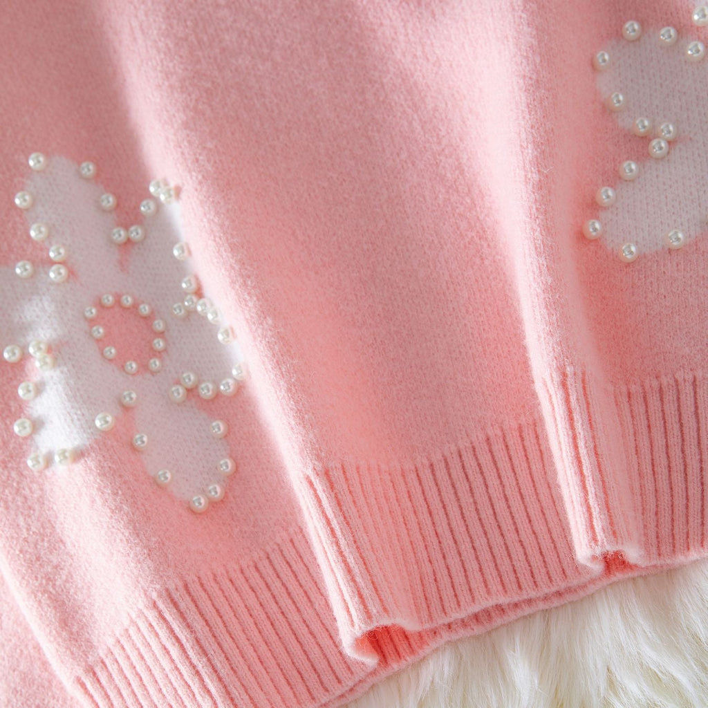 Close-up of a pink knitted scarf with white heart patterns and pearl embellishments on a fluffy white surface.