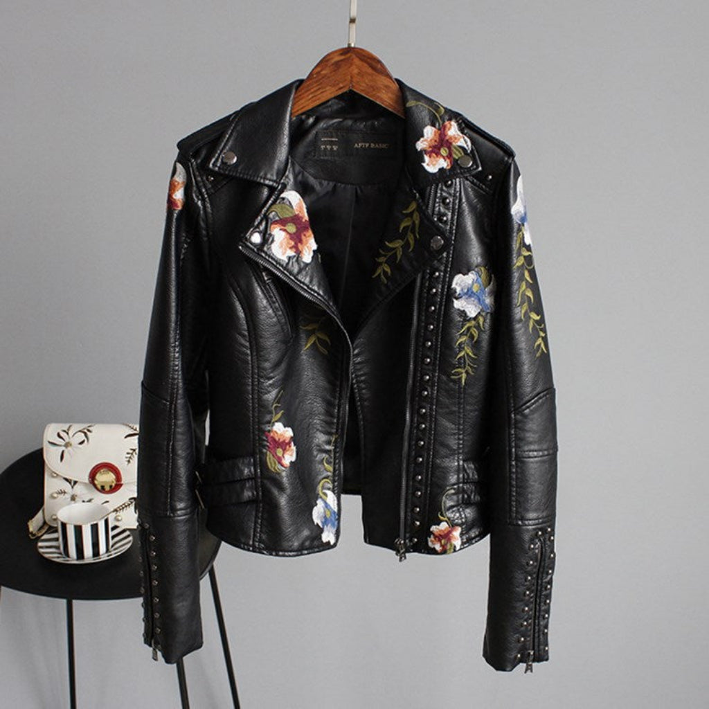 Black leather jacket with floral embroidery on a hanger against a gray background
