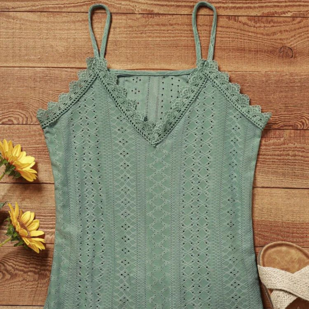 Green lace top on a wooden surface with yellow flowers and a sandal.