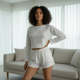 Woman sitting on a white couch wearing a white outfit in a bright room.
