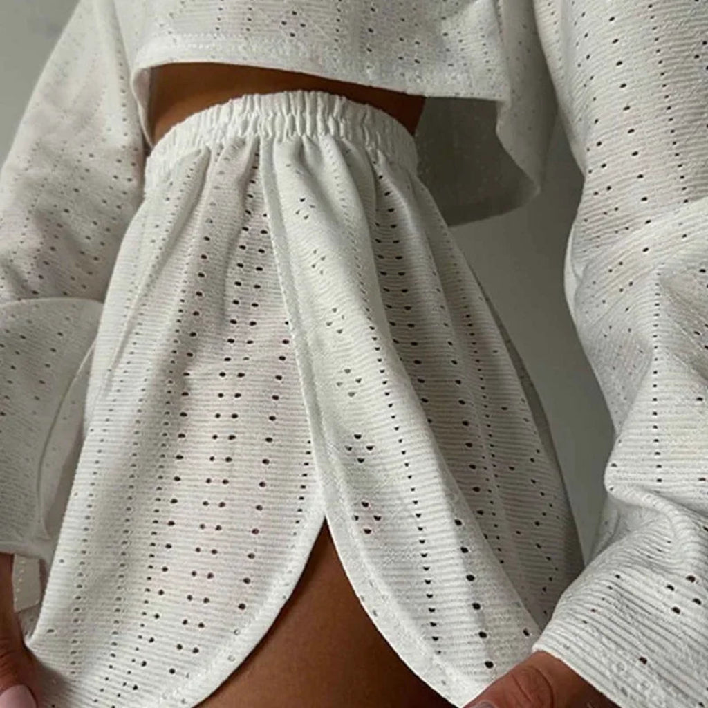 White perforated outfit with long sleeves and pants against a neutral background