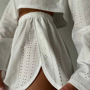 White perforated outfit with long sleeves and pants against a neutral background
