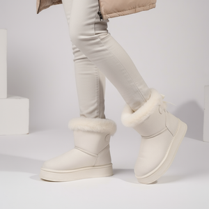 White winter boots with fur trim worn by a person on a light gray background