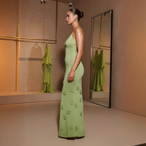 Woman in a green dress standing in front of a mirror in a room with beige walls.