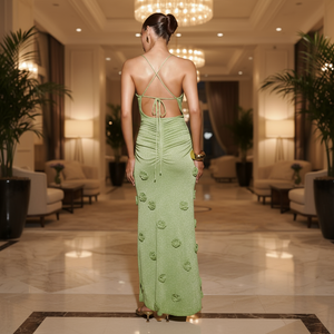 Woman in a green dress standing in an elegant indoor setting with chandeliers and plants.
