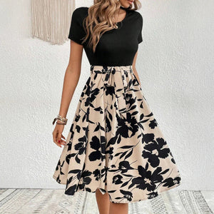 Woman wearing a black top and floral skirt against a white wall.