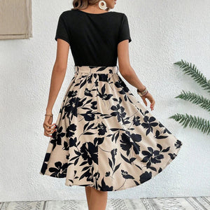 Woman wearing a black top and floral skirt against a white wall.