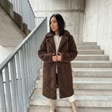 Woman wearing a brown teddy coat standing on concrete stairs.