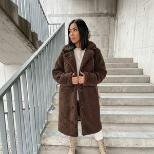 Woman wearing a brown teddy coat standing on concrete stairs.