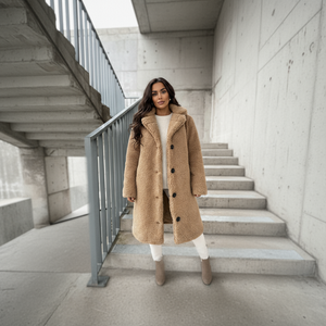 Woman in a beige coat standing on concrete steps in an urban setting
