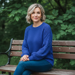 Woman in a blue sweater sitting on a bench with greenery in the background
