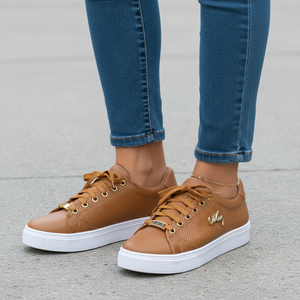 Brown sneakers with white soles worn with blue jeans on a gray pavement.
