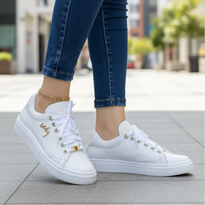 White sneakers with gold accents worn by a person on a blurred outdoor background