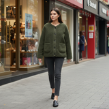Woman walking on a sidewalk wearing a green jacket and dark pants.