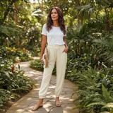 Woman walking through a lush garden wearing a white t-shirt and beige pants.