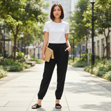 Woman in a white t-shirt and black pants standing on a sidewalk with trees and buildings in the background