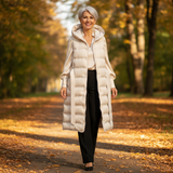 Woman in a long white puffer coat walking in an autumn park.