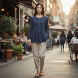 Woman in a blue shirt and beige pants standing on a city street with blurred background