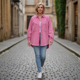 Woman wearing a pink denim jacket and blue jeans walking on a cobblestone street.