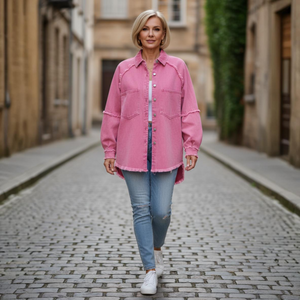 Woman wearing a pink denim jacket and blue jeans walking on a cobblestone street.