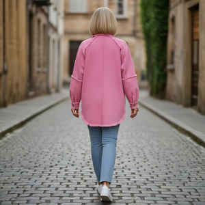 Person wearing a pink jacket walking down a cobblestone street.