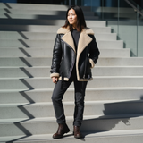Woman wearing a black shearling jacket with beige lining standing on outdoor steps.
