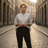 Woman wearing a beige button-up blouse and black trousers standing on a cobblestone street at sunset.
