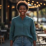 Woman wearing a teal button-up blouse and jeans standing outdoors with string lights in the background.