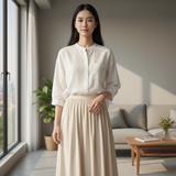 Woman wearing a white button-up blouse and beige skirt standing in a bright living room.