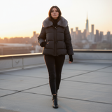 Woman in a black puffer coat with fur collar on a rooftop with city skyline in the background