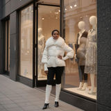 Woman in a white puffer jacket standing outside a store with mannequins inside