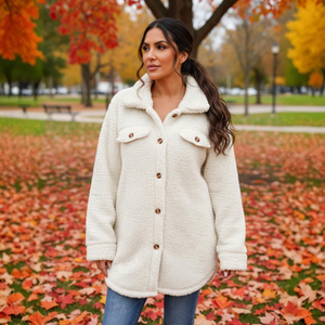 Woman wearing a white coat standing in an autumn park with colorful leaves on the ground.