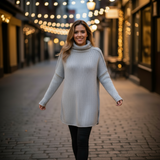 Woman in a light gray sweater walking on a street with string lights in the background