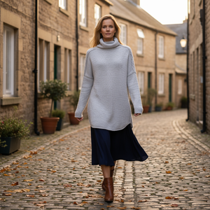Woman walking down a cobblestone street wearing a long light gray sweater and dark skirt.