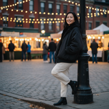 Woman leaning against a lamp post in an outdoor market setting with blurred people and lights in the background.