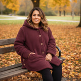 Woman in a purple coat sitting on a bench in an autumn park.