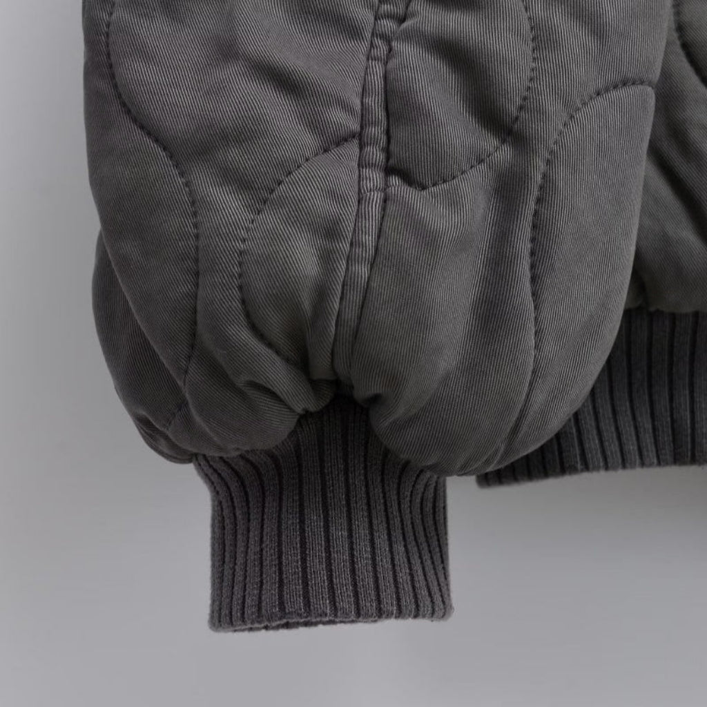 Close-up of a gray quilted jacket sleeve on a light gray background