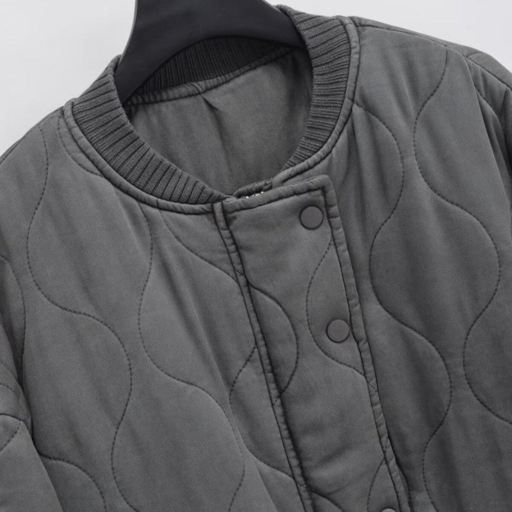 Gray quilted jacket on a hanger against a light gray background
