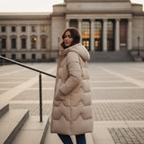 Woman in a long beige coat standing in front of a large building with columns.