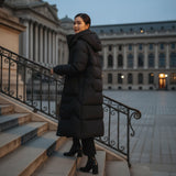 Woman in a long black coat standing on steps in front of a large building