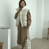 Woman wearing a beige puffer vest over a brown outfit, holding a tote bag indoors.