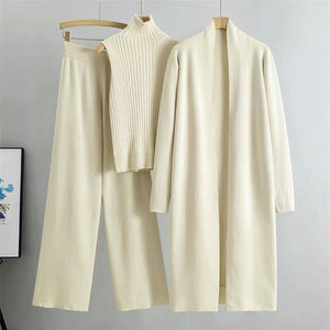 Beige outfit with a sweater, pants, and cardigan on hangers against a gray background.
