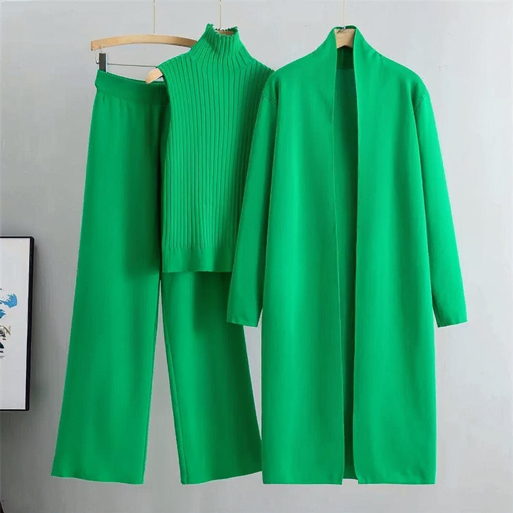 Green outfit with coat, pants, and sweater on hangers against a gray background